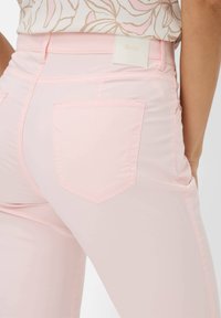 Lichtroze denim jeans met een hoge taille, twee achterzakken en een wit label met "Brax" op de achterkant van de tailleband. Glad textuur.