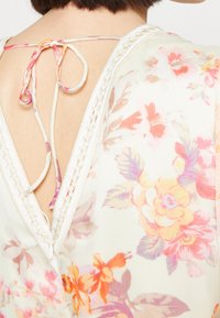 Détail d'une blouse florale avec un col en V et un dos ouvert, fermée par un lien tressé. Tissu doux et léger dans des tons pastels avec des motifs floraux.