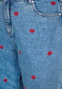 Svetlo modri denim različni z neenakomerno razporejenimi rdečimi izvezenimi ustnicami. Klasičen stil s petimi žepi in kovinskim gumbom ter zadrgo.