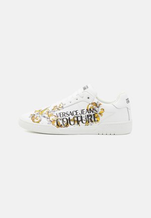 Weißer Sneaker mit niedrigem Schaft, goldenem Barockmuster und schwarzem "Versace Jeans Couture" Text an der Seite, weißen Schnürsenkeln und Gummisohle.
