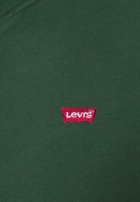 Tessuto verde scuro con una piccola toppa rossa del logo Levi's cucita vicino al centro.