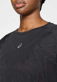 Μαύρο αθλητικό μπλουζάκι με γεωμετρικό σχέδιο, στρογγυλή λαιμόκοψη και υφασμάτινη υφή με αεριζόμενες λεπτομέρειες από δίχτυ. Λογότυπο στο στήθος.