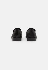 Mustat loafersit, joissa on rei'itetty nahka-yläosa, pyöreä kärki ja tasapohjat. Ominaisuuksia ovat suorat reunat ja yksinkertainen muotoilu ilmanvaihtoa varten.