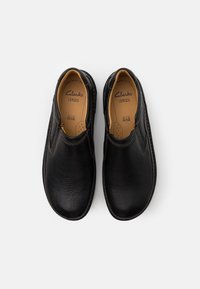 Schwarze Leder-Schlupfschuhe mit strukturiertem Obermaterial, elastischen Seitenteilen und dezenten Nähdetails. Das Innenfutter bietet gepolsterten Komfort.