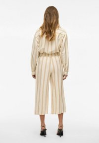 Beige un krēms svītrainā žakete ar atbilstošām culotte biksēm. Brīvas formas, plaši kājiņas un elastīga josta. Melni ar augstu papēdi sandales noslēdz izskatu.