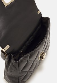 Czarna skórzana torebka z pikowaną fakturą, złotymi akcentami metalowymi oraz otwartym wierzchem, odsłaniającym podszyte wnętrze z kieszenią na zamek.