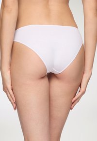 Slip bikini in cotone bianco con design senza cuciture, vita bassa e texture liscia, mostrato da dietro con copertura minima.