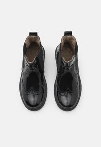 Bocanci negri din piele lacuită, cu detalii brogue, panouri elastice pe lateral și căptușeală din lână texturată. Prezintă o talpă din cauciuc rezistentă.