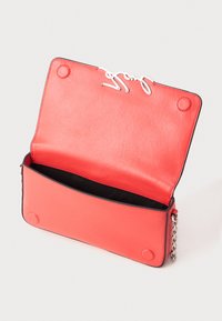 Sarkanas ādas roku soma ar sudraba ķēdes siksniņu, atvērtā vāciņā ir magnētiskās pogu aizdares un melns iekšējais oderējums.