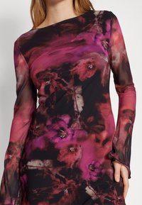 Robe à manches longues en tissu transparent avec un fond noir agrémenté de grands motifs floraux roses et rouges. Encolure asymétrique et manches ajustées.