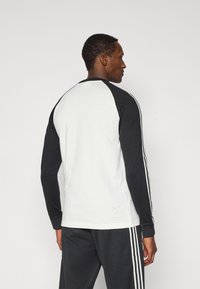 Μπλούζα με μακριά μανίκια σε ασπρόμαυρο χρωματικό συνδυασμό. Βαμβακερό μείγμα, σχέδιο raglan, με ριγέ λεπτομέρειες και μικρό λογότυπο στο κάτω μέρος.