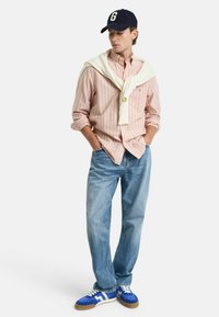 Lichte outfit met een lichtroze gestreepte shirt, lichtblauwe denim jeans, een witte trui over de schouders gedrapeerd en blauwe sneakers.