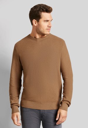 Brauner strukturierter Pullover mit Rundhalsausschnitt, gerippten Bündchen und Saum. Der Stoff hat ein dezentes Muster und wird über grauen Jeans getragen.