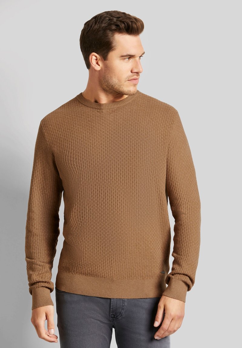 Brauner strukturierter Pullover mit Rundhalsausschnitt, gerippten Bündchen und Saum. Der Stoff hat ein dezentes Muster und wird über grauen Jeans getragen.