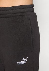 Svarta träningsbyxor med mjuk textur, som har en dragsko i midjan och en vit Puma-logotyp på vänster ben.