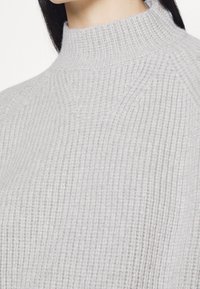 Grå ribbad polotröja med hög krage och texturerat tyg, med en figurnära silhuett och subtila sömdetaljer.