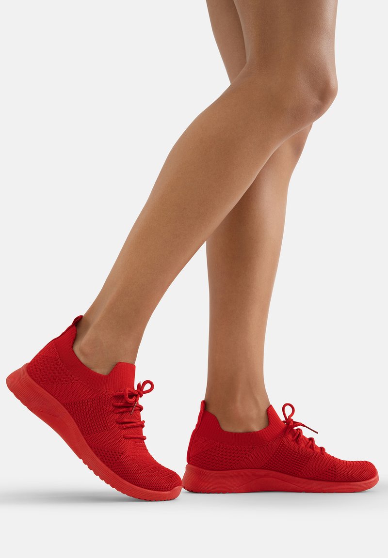 Rote Turnschuhe mit einem gestrickten Obermaterial, die ein niedriges Knöchel-Design, eine Schnürung und strukturierte Akzente an den Seiten aufweisen.