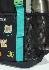 Čierna taška so tyrkysovým popruhom, sieťovaná kapsa obsahujúca striebornú fľašu Adidas na vodu a pixelové farebné nálepky na látke.