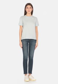 Maglietta azzurra chiara a maniche corte in cotone morbido, con colletto rotondo e logo ricamato; abbinata a jeans skinny scuri e sneakers.