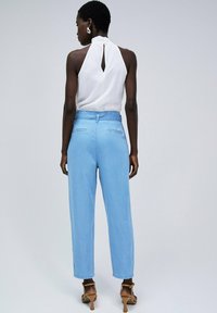 Pantalones de mezclilla azul claro con cintura alta y dos bolsillos traseros. Combinados con una blusa blanca sin mangas que tiene un detalle de ojal.