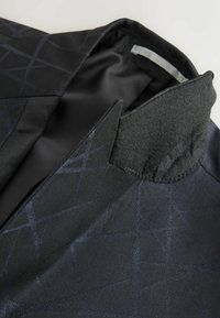 Schwarze Jacke mit geometrischem Muster, aus glattem Stoff gefertigt. Verfügt über einen strukturierten Kragen und eine glatte Fütterung in dunklen Farbtönen.