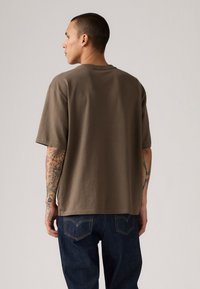 Braunes Baumwoll-T-Shirt mit lockerer Passform, kurzen Ärmeln und Crew-Ausschnitt. Merkmale sind sichtbare Nähte und ein Saumtag.
