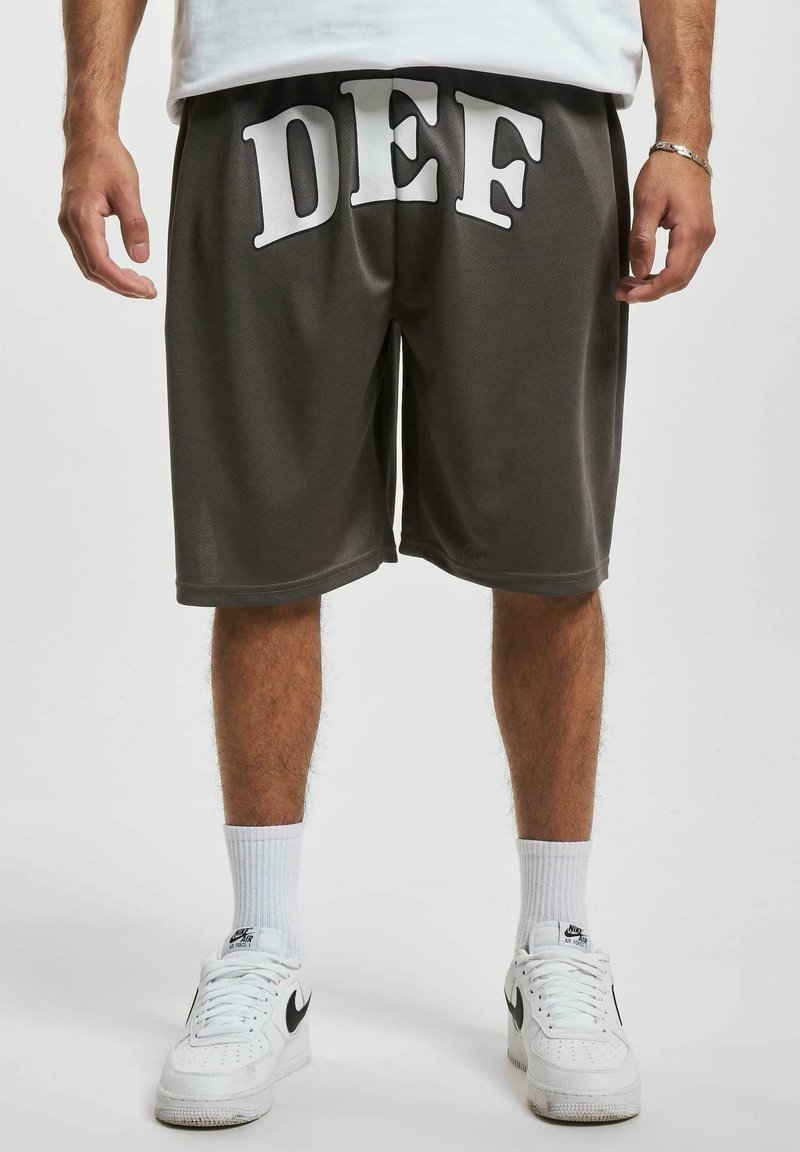 Grå treningsshorts med hvit påskrift "DEF" på framsiden, laget av et lett materiale. Kombinert med hvite sneakers og sokker.