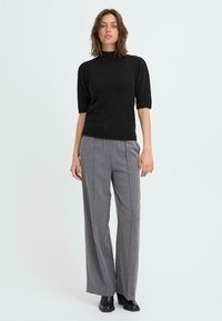 Sort kortærmet turtleneck sweater parret med lysegrå vidde bukser og sorte ankelstøvler. Enkeltfarver, bløde teksturer og skræddersyet pasform.