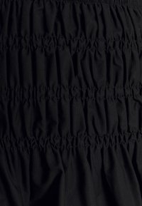 Svart tyg med insamlade sektioner som visar en strukturerad yta. Materialet verkar mjukt, lätt och faller fluidiskt med elastiska detaljer.