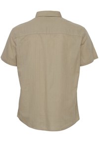 Camisa de manga corta beige hecha de tejido ligero, con cuello de punta, corte recto y una sutil textura vertical.