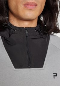 Felpa con cappuccio nera, corpo grigio, apertura frontale a mezza zip e lacci regolabili. Presenta un piccolo logo sulla parte anteriore.