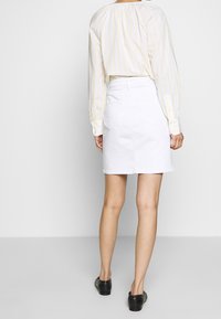 Bílé denimové sukně s přiléhavým pasem, předními a zadními kapsami a rovnými liniemi, v kombinaci s dlouhým rukávem košile s žlutými a bílými pruhy.