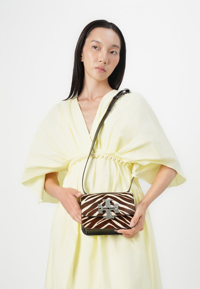 Brązowa i biała paskowana torba na ramię z logo w kolorze srebrnym, z klapką i paskiem na ramię. Gładka skóra i teksturowany materiał.