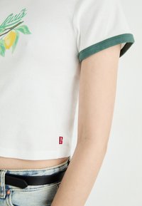 Vit kortärmad t-shirt med grön kant, med en citron-graphic. Röd Levi's-logotyp synlig på sidan. Jeansshorts och svart bälte ingår.
