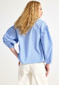 Blå og hvid stribet oversized skjorte med ballonærmer, lavet af et glat stof. Kantlinjen er let buet med en løs pasform.