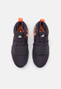 Dark purple athletic shoes with orange accents and a black perforated strap. Features a textured upper and white rubber sole.