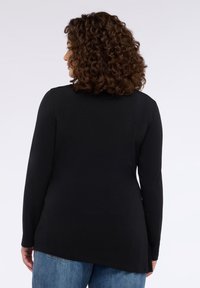 Czarna bluzka na długi rękaw wykonana z miękkiego materiału, z zakrzywionym dołem i zaokrąglonym dekoltem, noszona na jasnoniebieskich dżinsach.