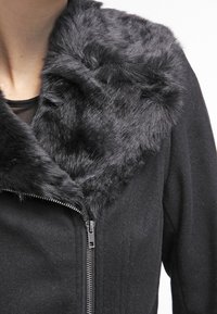 Svart jacka med fuskpälskrage, med dragkedjestängning. Strukturerad tyg med en slät yta och mjuk, fluffig krage.