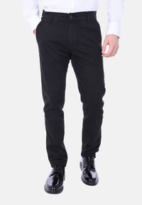Chinos neri in cotone, con una vestibilità slim, chiusura con bottone e tasche laterali. Indossati con scarpe nere lucide.