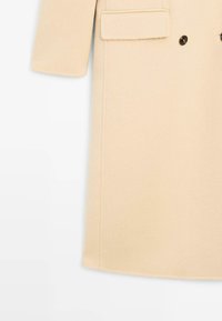 Beige uldfrakke med lige snit, der har dobbeltknappet design, lukning med to knapper og en påsyet lomme på venstre side.