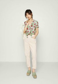 Blusa floral de manga curta com cores verde, rosa e branca; calças rosa claro de cintura alta; saltos plataformas verdes; acessórios mínimos.