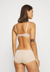 Set di lingerie beige, composto da un reggiseno liscio con spalline regolabili e chiusura a gancio, abbinato a slip hipster coordinati.