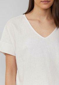 Witte linnenblouse met een V-hals en korte mouwen. De stof heeft een zachte textuur, met een subtiel geweven patroon.