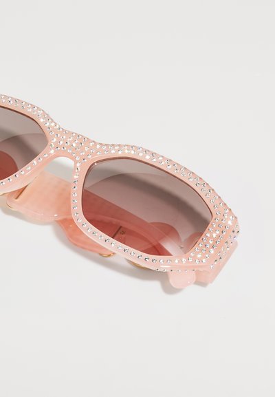 Óculos de sol cor-de-rosa com um design robusto, adornados com strass transparentes. As lentes são degradê, passando de tons claros para mais escuros.