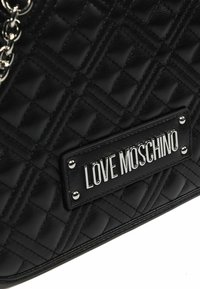 Schwarze, gesteppte Handtasche aus Kunstleder mit silberner Kettendetailierung, ausgestattet mit einem auffälligen "LOVE MOSCHINO" Logo-Plakette und Nietenakzenten.