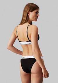 Svart bomull bralette og matchende truser med hvit Calvin Klein-logo på båndet, justerbare stropper, glatt tekstur og minimalistisk design.