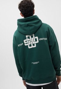 Sudadera verde con capucha, que presenta el texto blanco "STAY UNITED" y un diseño gráfico en la parte posterior. Puños y cintura acanalados.