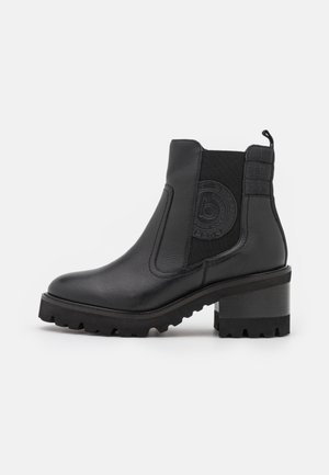 Bottine en cuir noir avec talon épais, panneau latéral élastique, languette de tirage et logo circulaire embossé sur le côté extérieur.