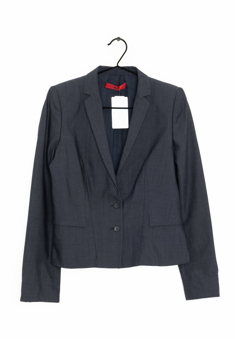 Tmavě šedý tailored blazer se dvěma knoflíky na přední straně, zavěšený na černém ramínku, s bílou cenovkou a červenou vnitřní nášivkou.