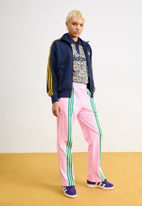 Námořnická bunda na zip se žlutými pruhy, barevné květované polo, růžové tepláky se zelenými pruhy a fialové tenisky s bílými detaily.